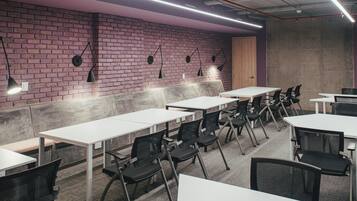 Un salón de conferencias con mesas blancas y sillas negras, una pared de ladrillo e iluminación fluorescente.