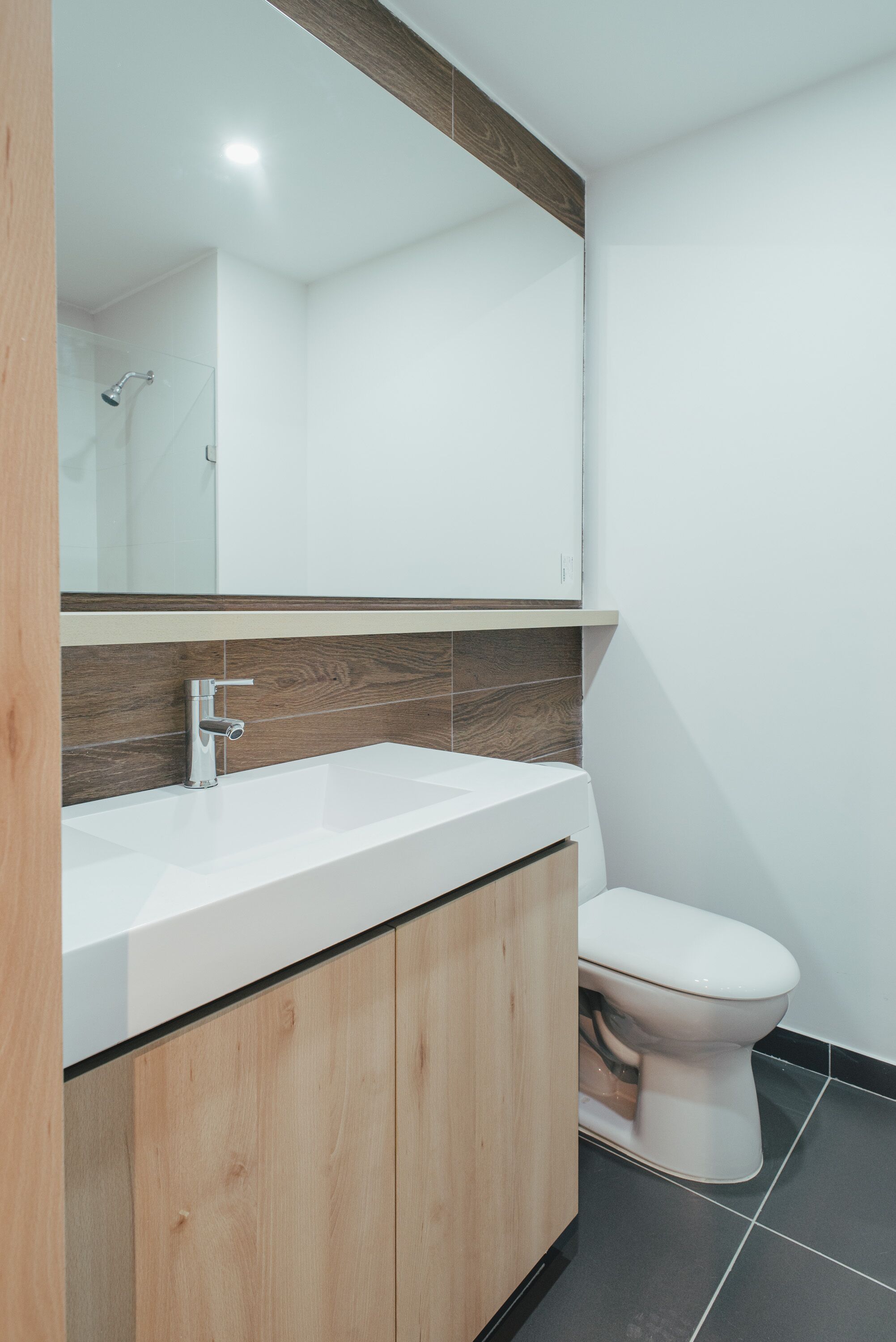Un baño moderno con un lavamanos blanco, armarios de madera, un inodoro blanco y un espejo sobre el lavamanos.