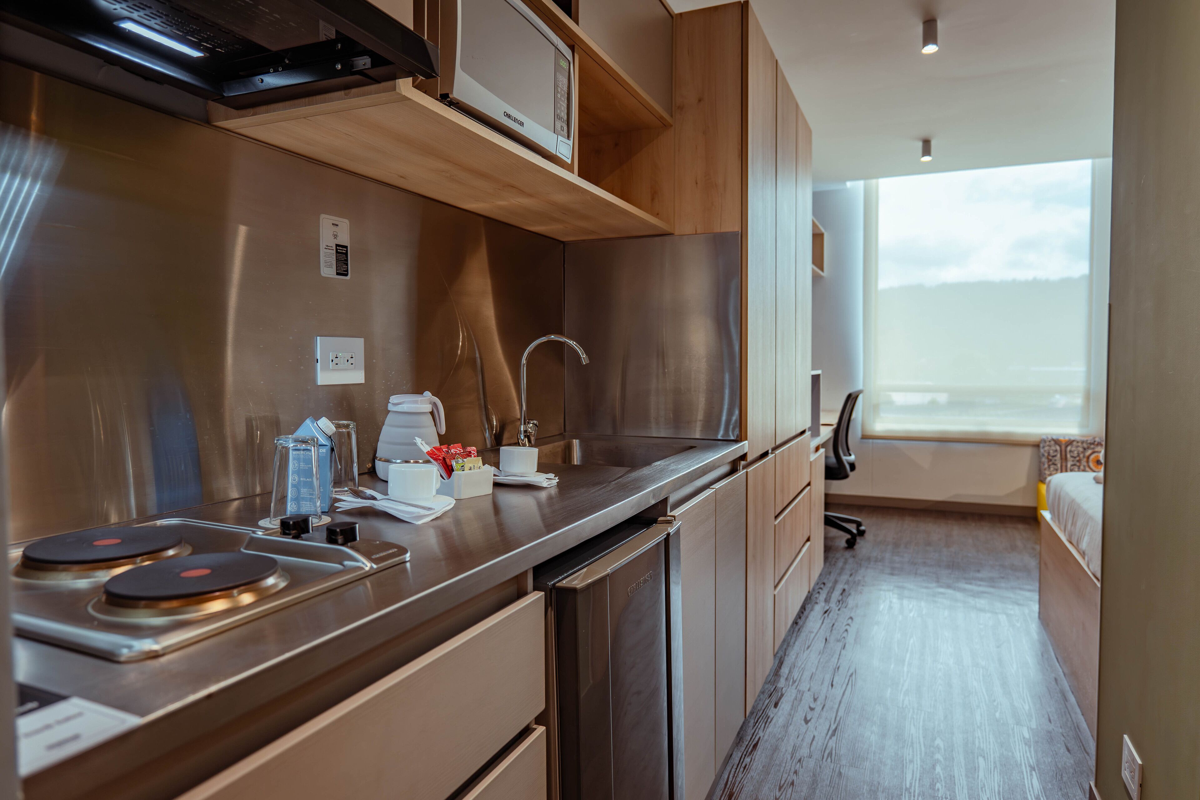 Une cuisine de taille réduite, dotée d’appareils électroménagers en acier inoxydable, de meubles de rangement en bois et d’une fenêtre offrant une vue sur l’extérieur.