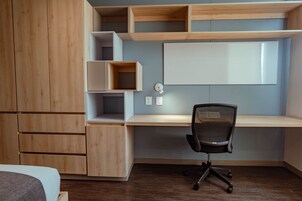Un dormitorio moderno con un armario de madera, un escritorio con silla y una cama.