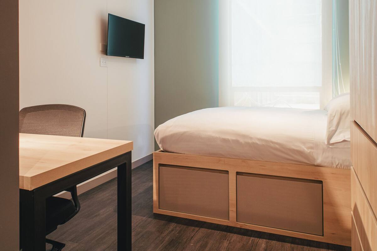A bedroom with a bed, a desk, and a TV mounted on the wall.