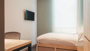 A bedroom with a bed, a desk, and a TV mounted on the wall.