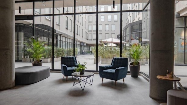 Un espai interior modern amb grans finestres, dos butaques blaves, una taula de centre rodona i plantes en testos.
