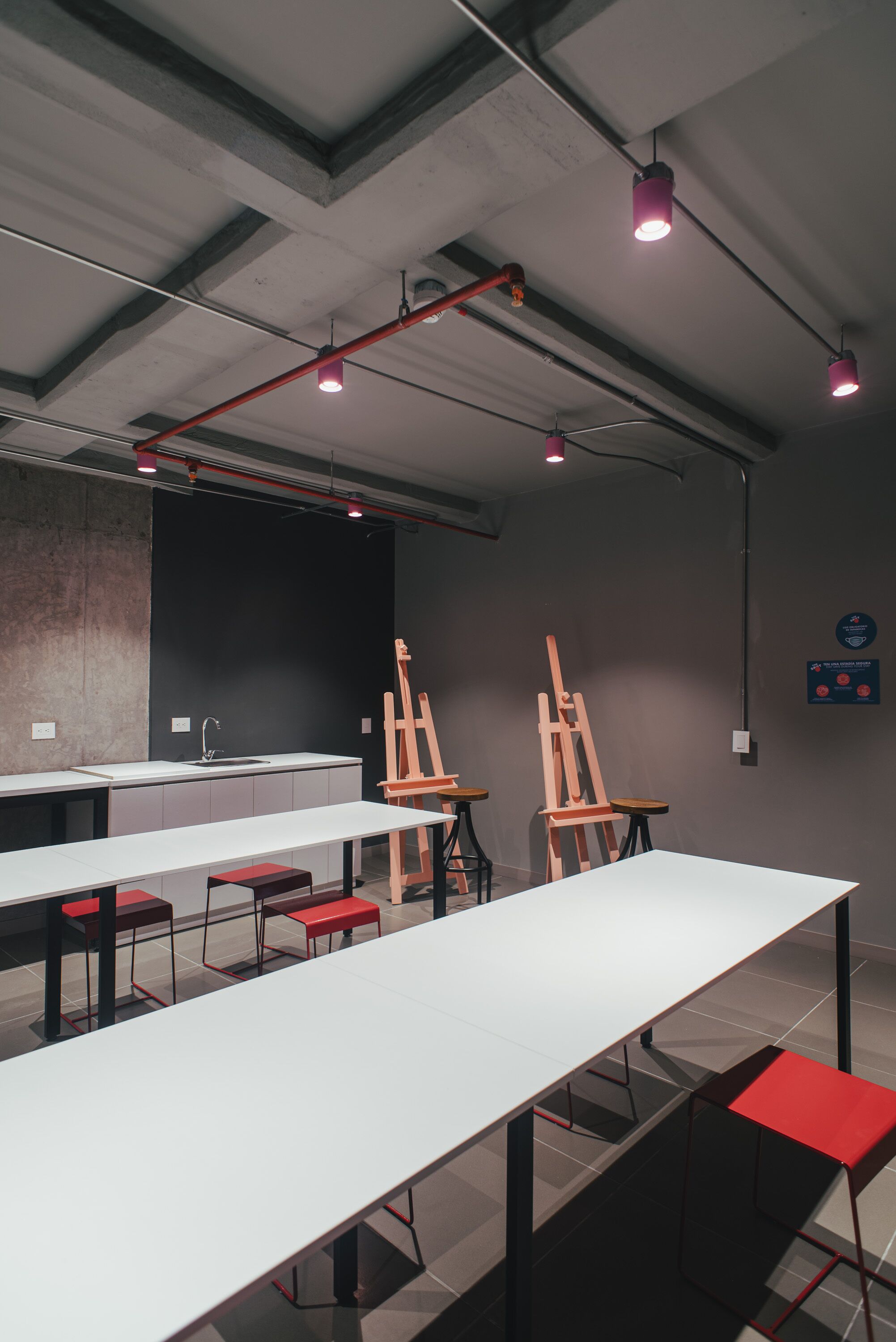 Eine moderne Kunstgalerie mit weißen Tischen, roten Bänken und Staffeleien.