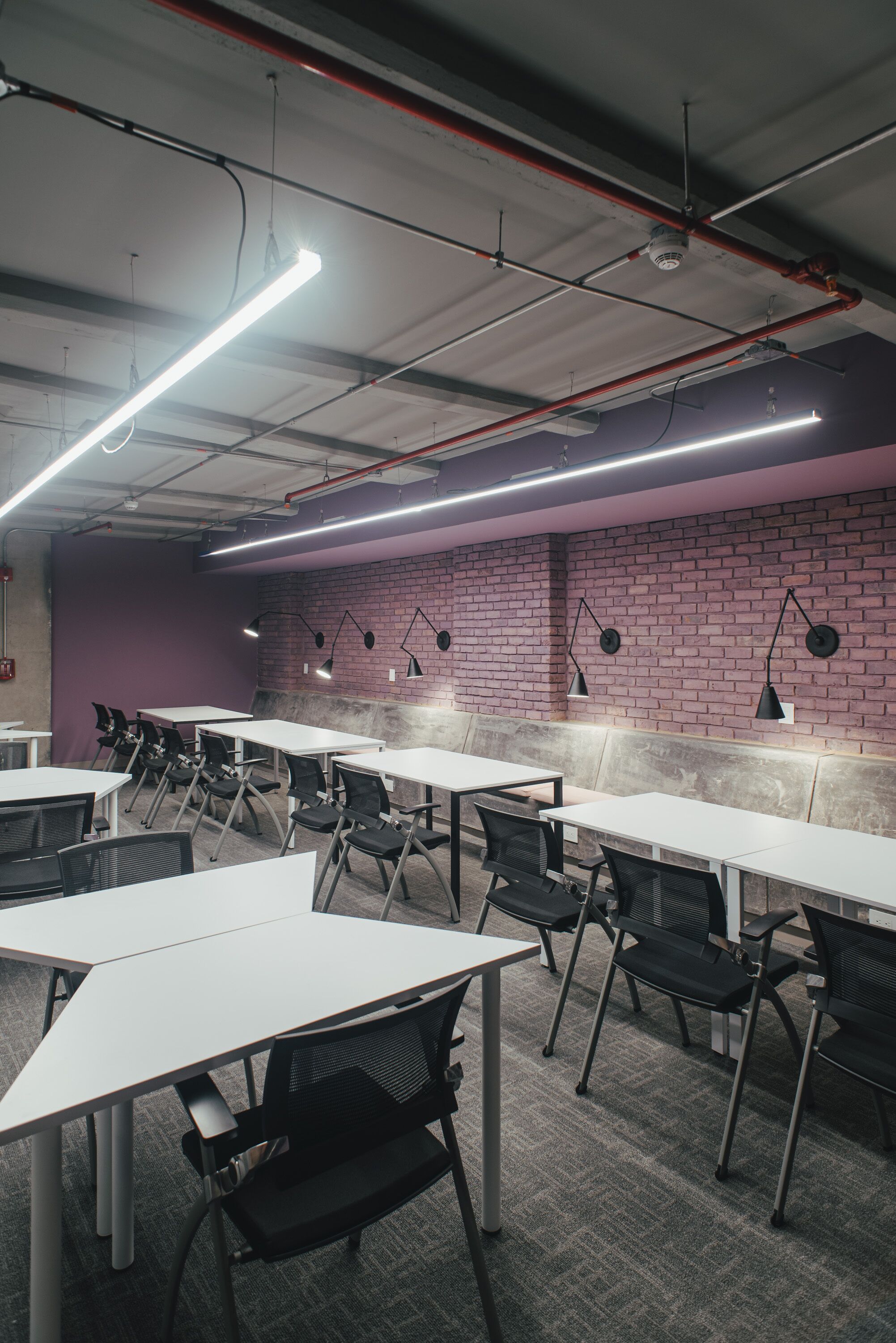 A conference room with white tables and black chairs, a brick wall, and overhead fluorescent lighting.