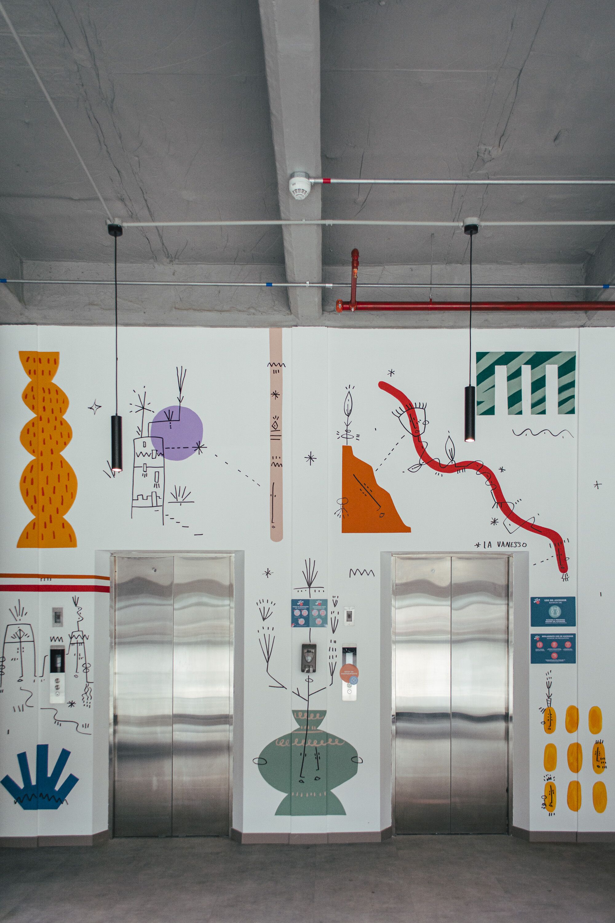 An elevator with a metallic interior and a wall with various abstract drawings and designs.