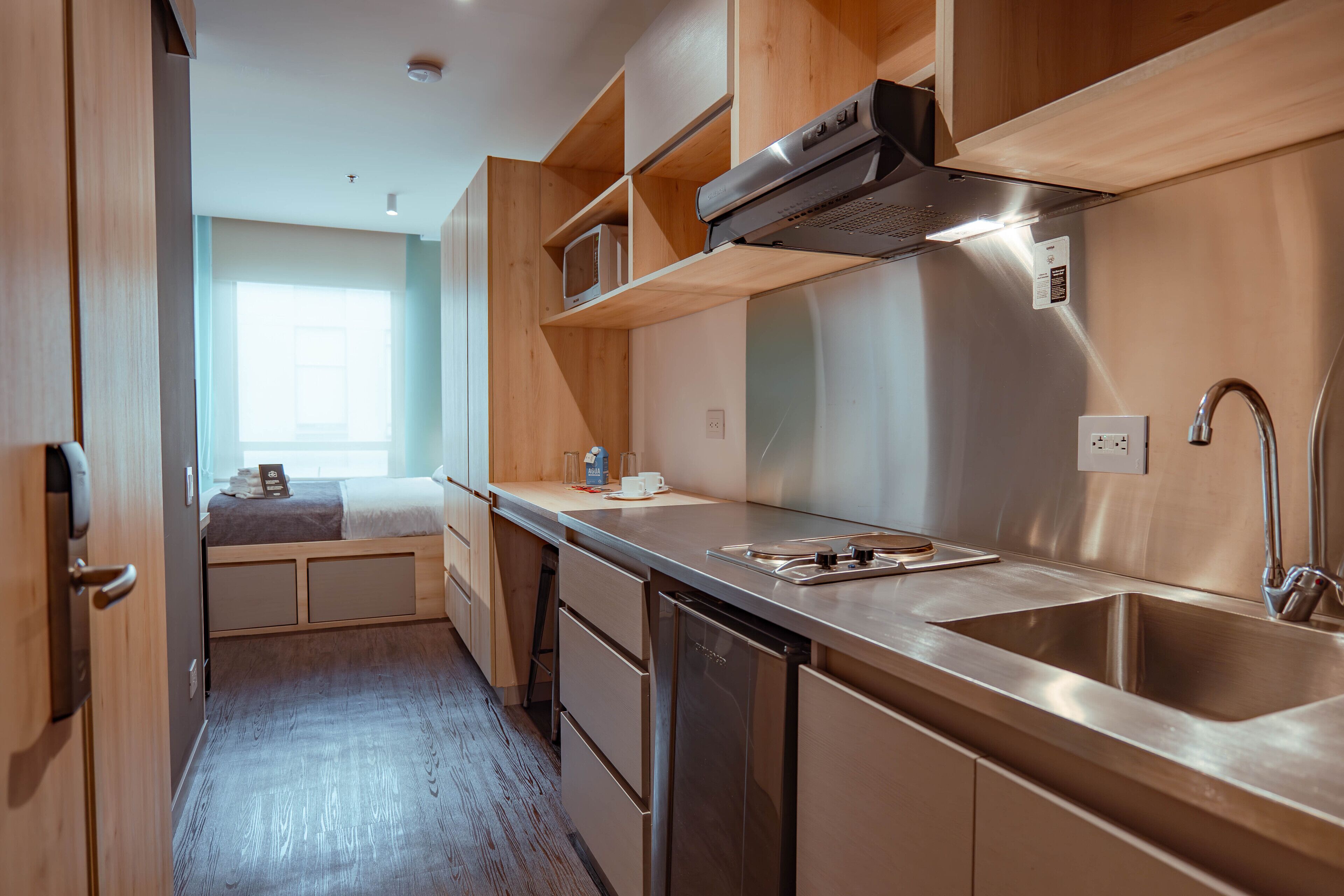 A compact kitchen with wooden cabinets, a stainless steel sink, and a microwave.
