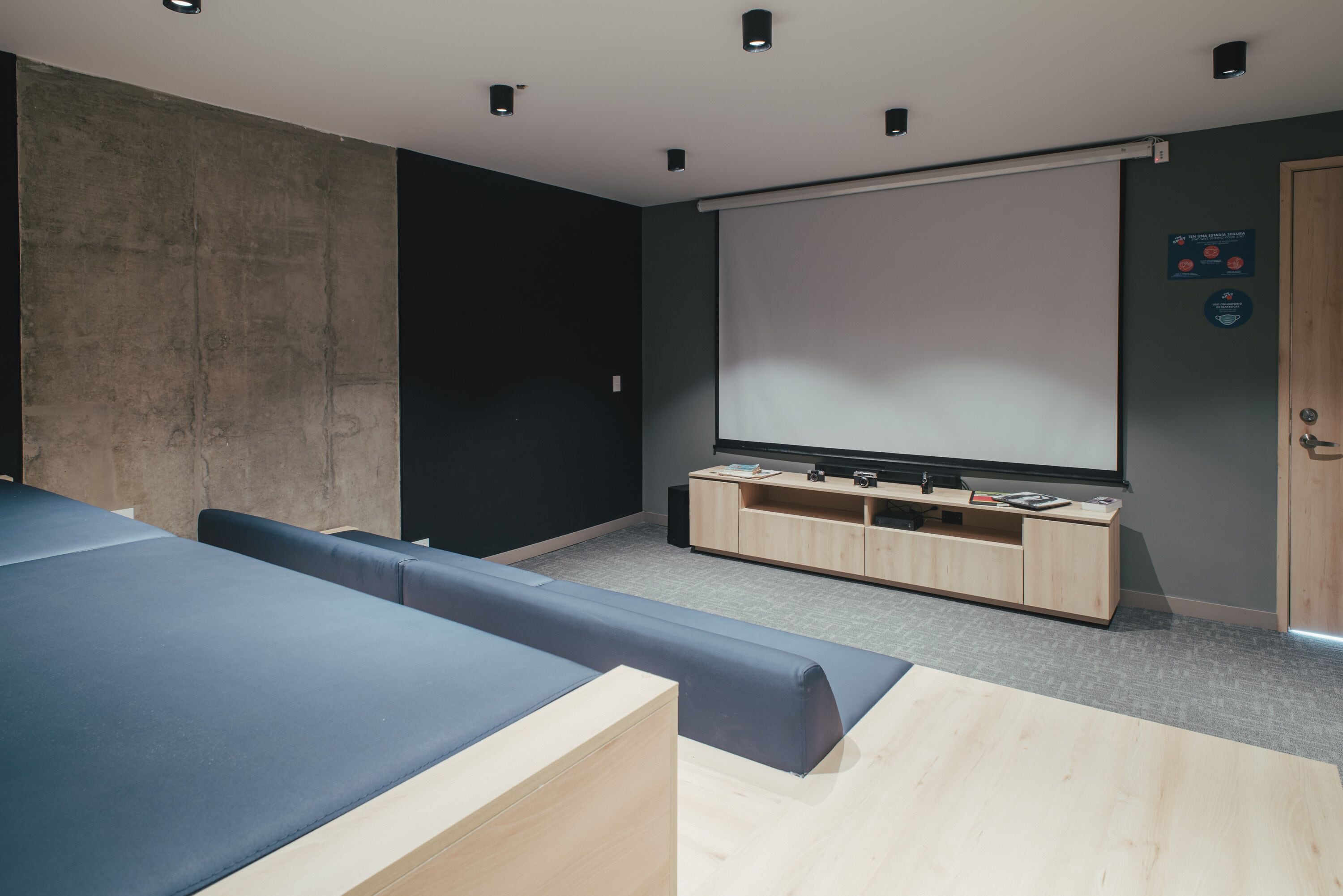 A modern room with a large screen, seating, and a wooden cabinet.