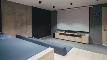 A modern room with a large screen, seating, and a wooden cabinet.