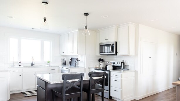 A modern kitchen with white cabinetry, a central island with two chairs, a microwave, and a kettle.