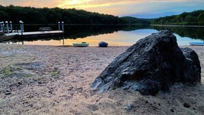 En stilla sjö med en brygga, en stor sten i förgrunden och en solnedgång i bakgrunden.