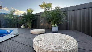 Una terraza de madera con asientos de mimbre redondos, una piscina pequeña y plantas en macetas.