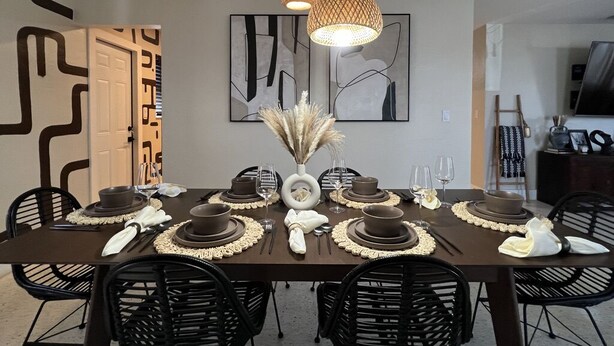 Comedor con una mesa marrón oscuro dispuesta para seis personas, sillas negras y una lámpara colgante moderna.