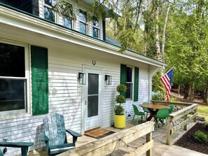 A house with a front porch, a dining table with chairs, a flag, and a potted plant. - Stonewall Christmas Cottage, Door County, Fire Pit, Coffee Bar - Sleeps 8 (Baileys Harbor)