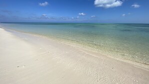 Uma praia com águas turquesa cristalinas e uma faixa de areia dourada sob um céu azul com algumas nuvens.