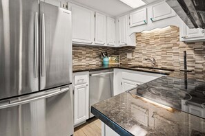 A modern kitchen with stainless steel appliances, white cabinetry, a herringbone tile backsplash, and a black granite countertop.