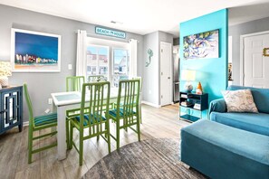 Un salon comprenant un coin repas, un canapé, un tableau et une enseigne sur laquelle on peut lire : « MAISON DE PLAGE ».