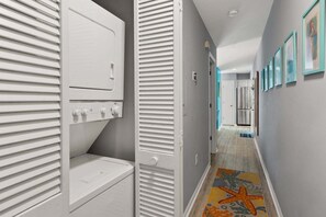 Un couloir avec un tapis à motifs, une porte dotée d’une poignée et un réfrigérateur à l’arrière-plan.