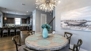 A dining area with a round wooden table, chairs, a vase with flowers, and a modern chandelier.