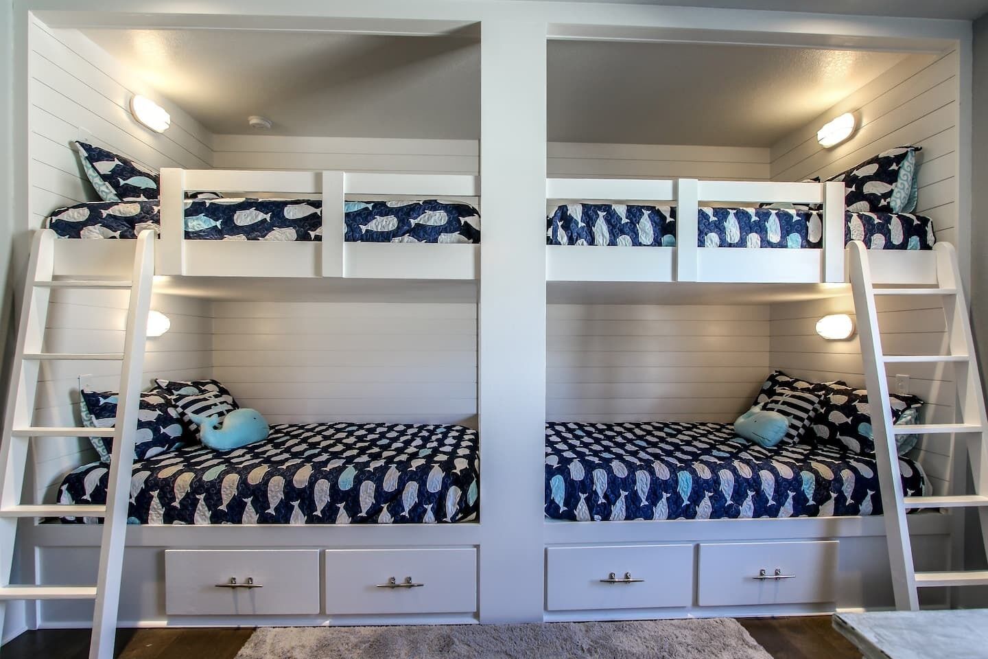 A room with two bunk beds, each with a ladder, and a small desk with drawers.