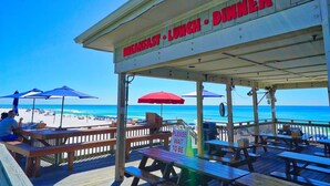 A beachside restaurant with a sign indicating breakfast, lunch, and dinner services.