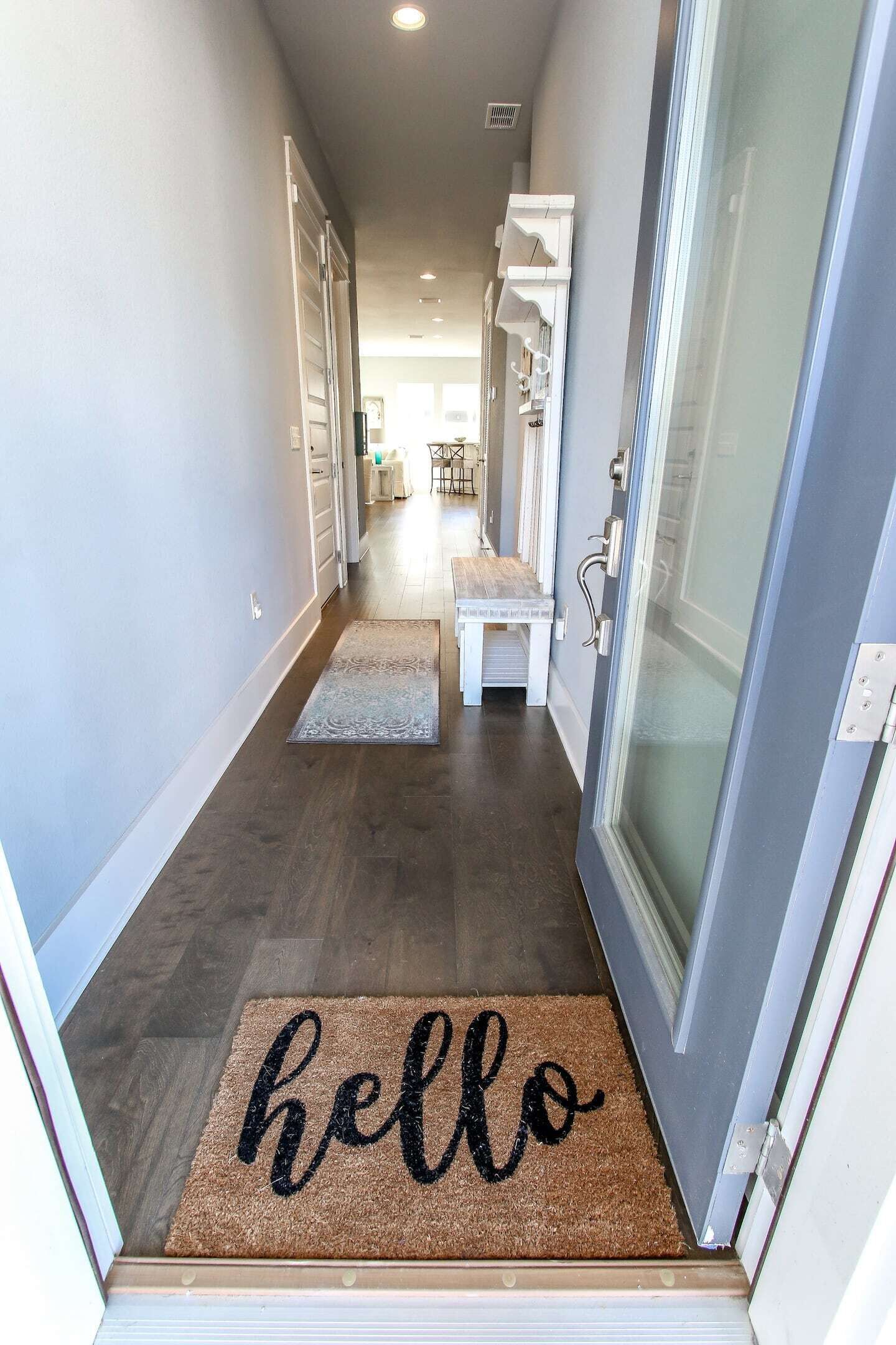A hallway with a doormat reading "hello" leading to a room with a glass door.