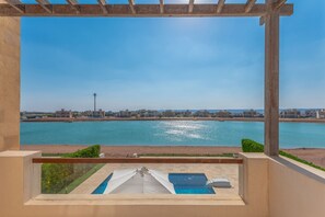 Un balcon offrant une vue sur une vaste étendue d’eau, une piscine et un paysage urbain au loin.