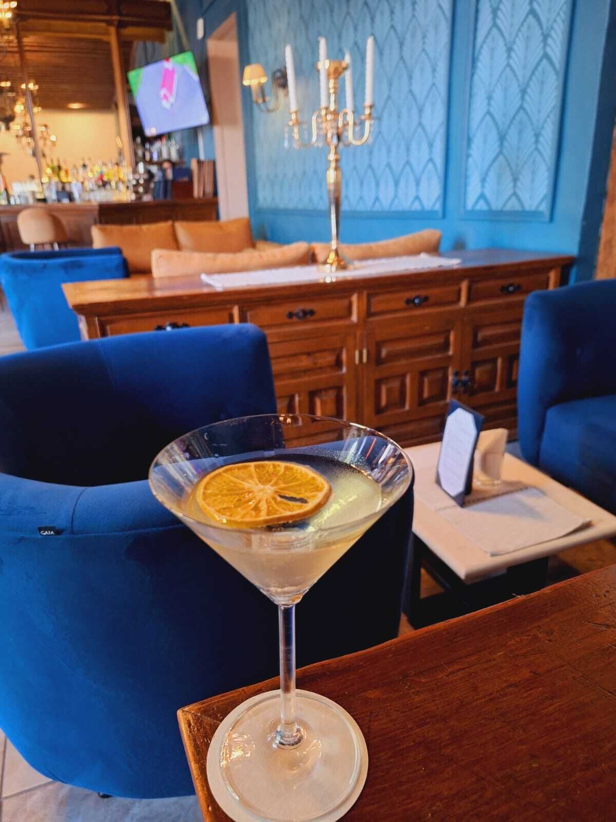 A bar area with blue chairs, a wooden table with a martini glass, and a television in the background.