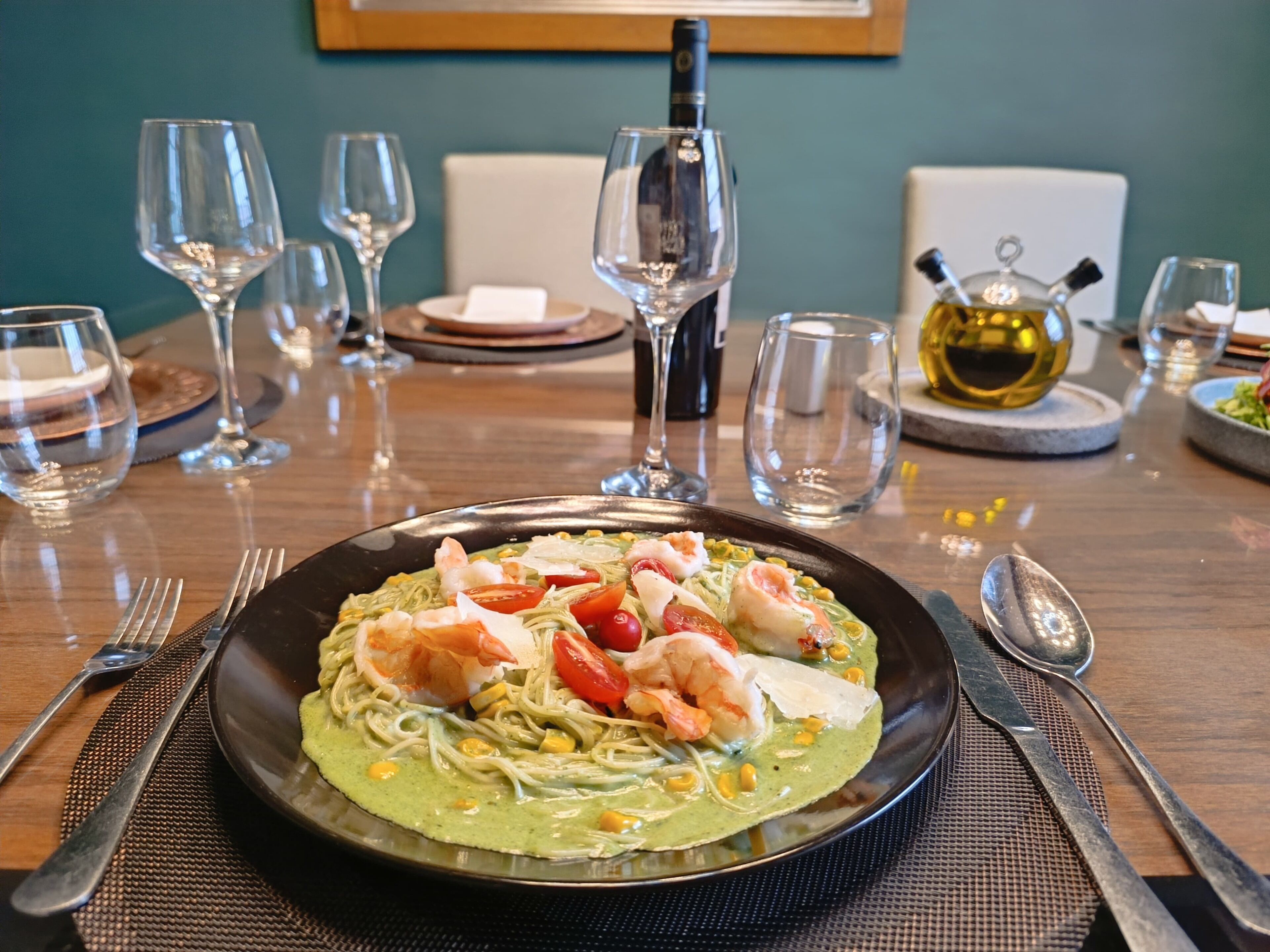 Una mesa dispuesta con un plato de pasta, copas de vino y una botella.