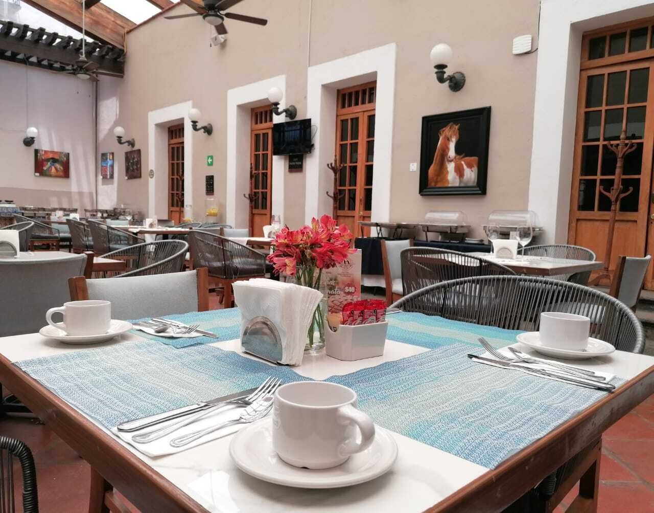 A restaurant with tables set for dining, featuring a blue tablecloth, white plates, and a vase of flowers.