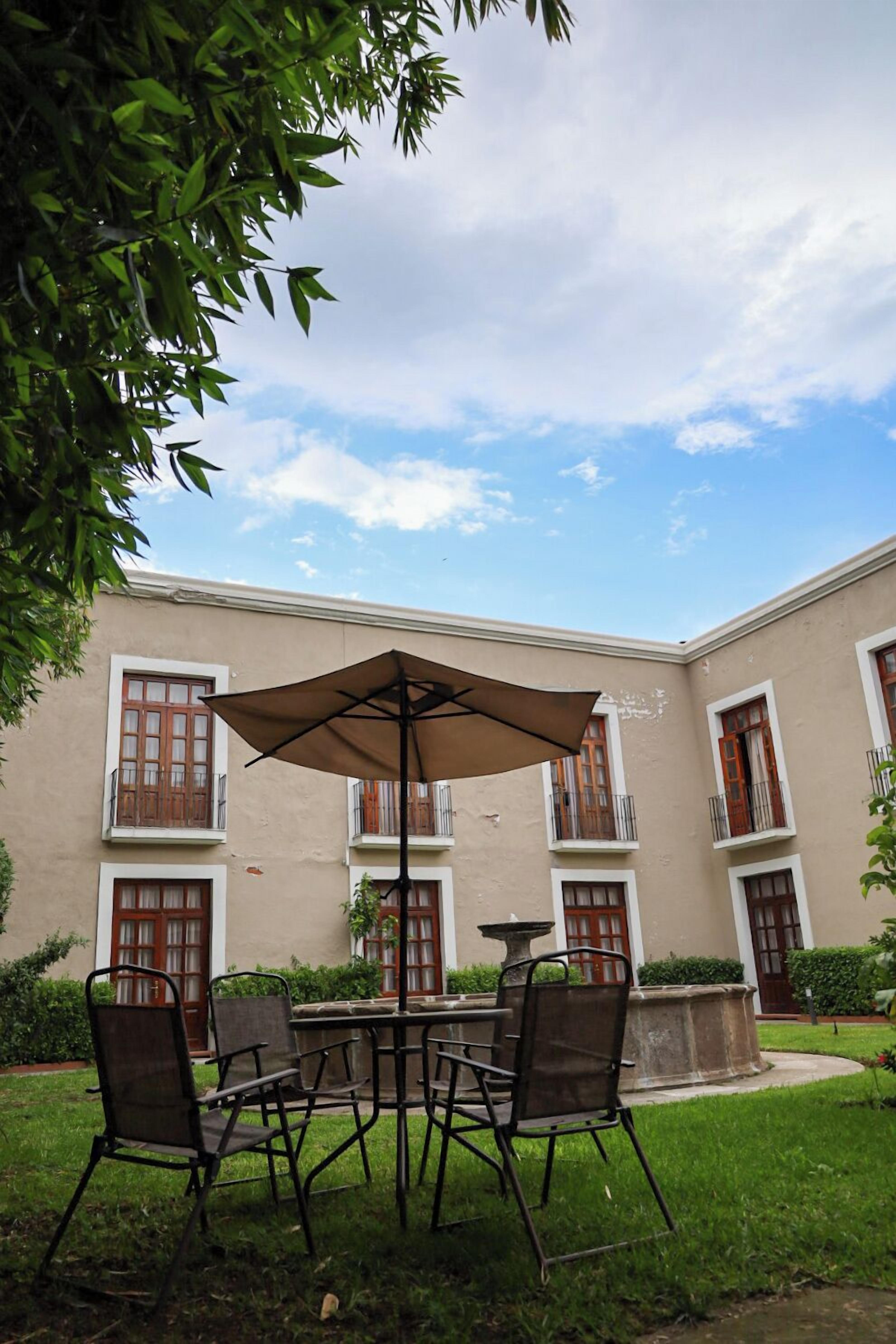A courtyard with a table and chairs under a large umbrella, surrounded by a building with multiple windows and balconies.