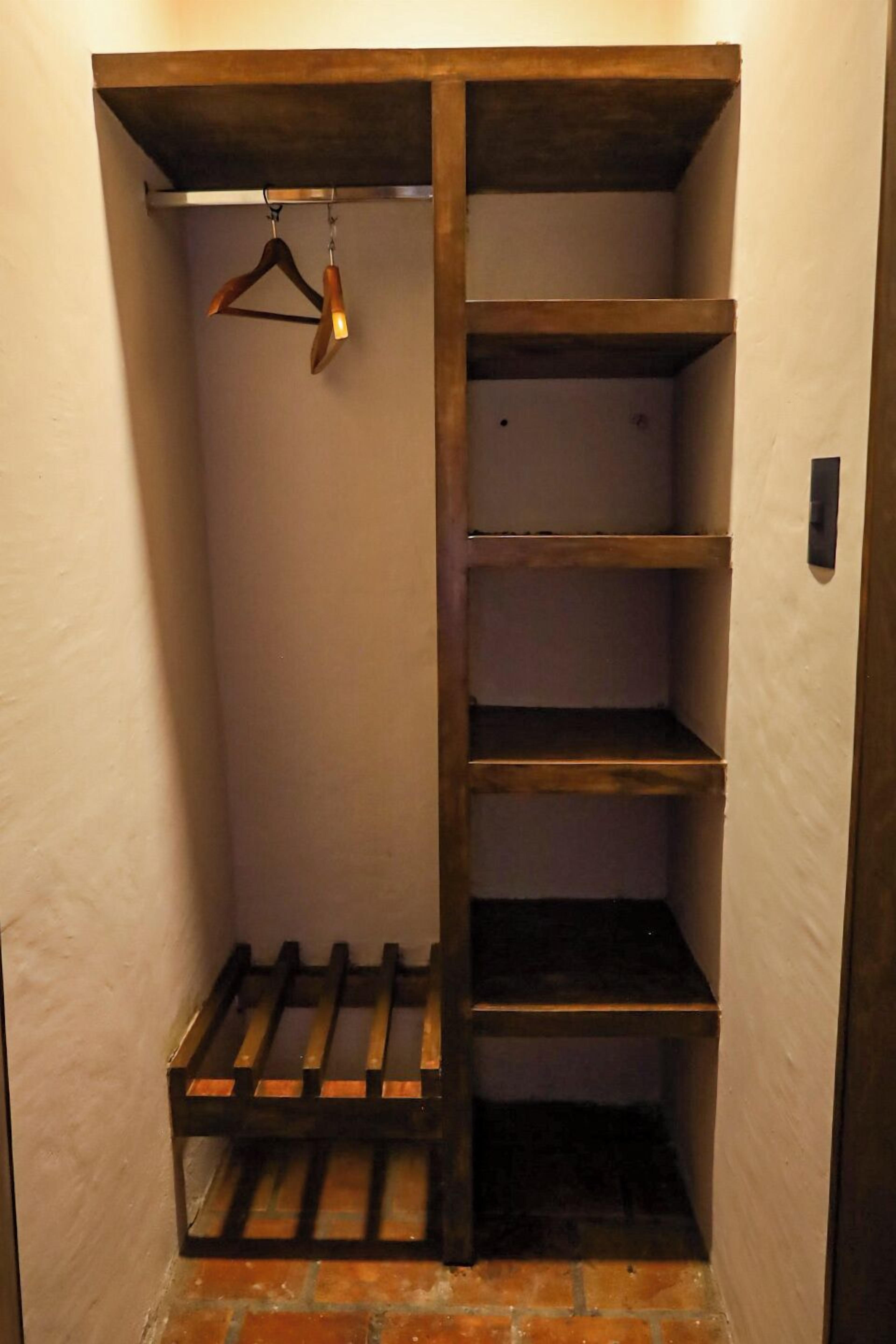 Un couloir étroit avec un placard en bois doté d’étagères ouvertes et d’une tringle pour suspendre les vêtements.
