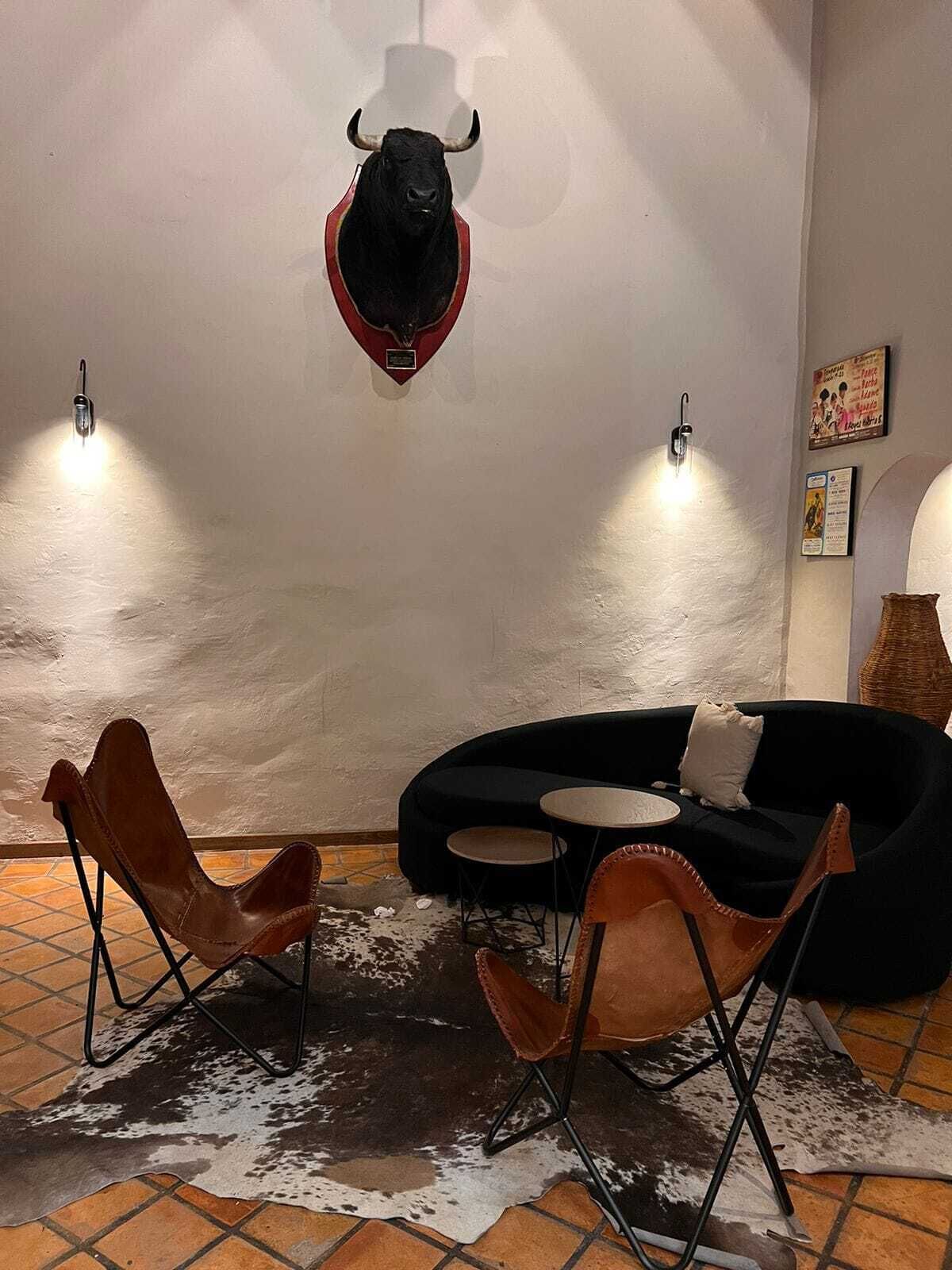 Una habitación con un sofá negro, dos sillones de cuero, una mesita redonda y un tapiz de piel de vaca.