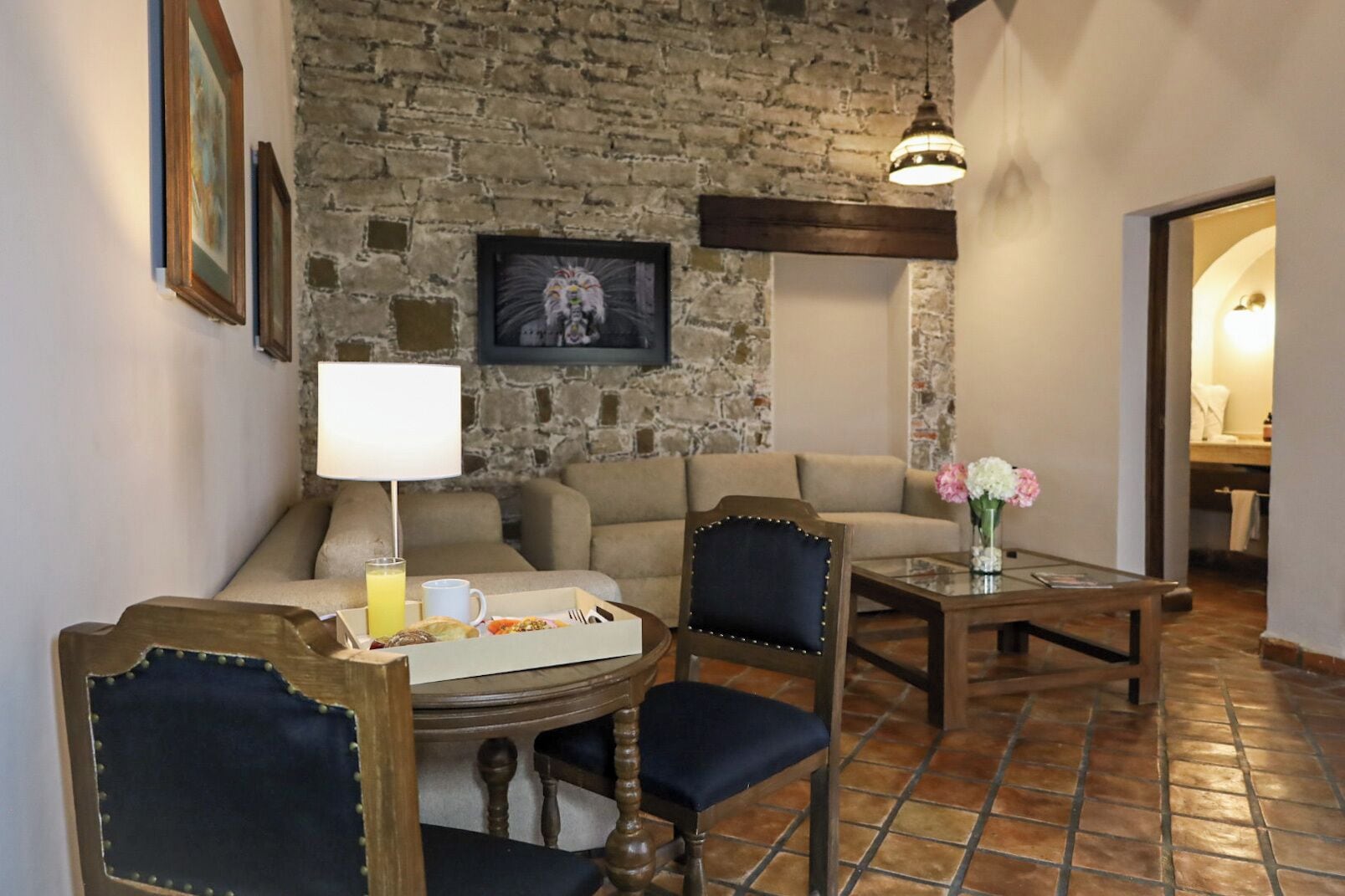 Una sala de estar acogedora con una pared de piedra, un sofá, una mesa de centro con un jarrón de flores y una mesa de comedor con sillas.