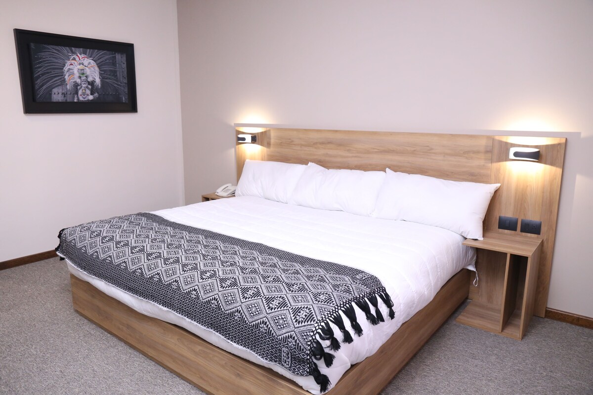 A neatly made bed with a patterned blanket, a wooden headboard, bedside lamps, and a framed picture on the wall.