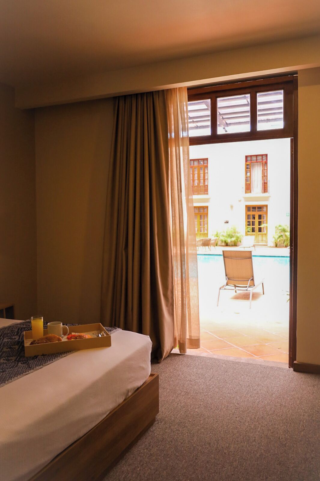 A hotel room with a bed, a tray with breakfast items, and a view of an outdoor pool area.