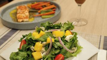 A plate of food with a salad and grilled fish, a glass of drink, and a pitcher of flowers on a table.