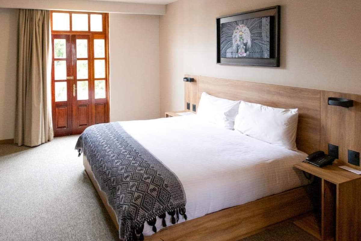 Un cuarto de hotel con una cama grande, un cabecero de madera, una mesita de noche con un teléfono y un cuadro enmarcado en la pared.