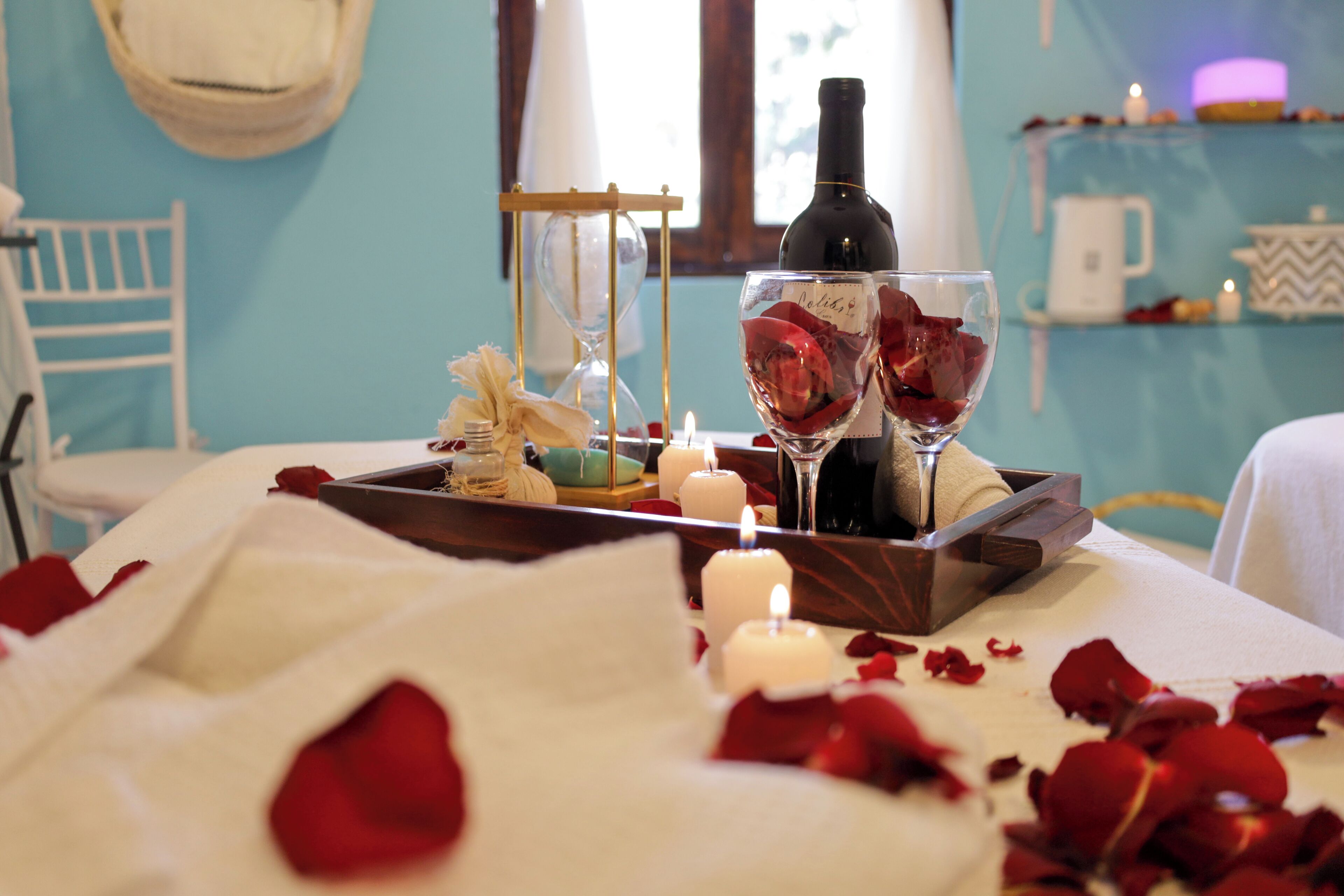 Ambiente romántico con una vela, pétalos de rosa y una botella de vino sobre una bandeja.