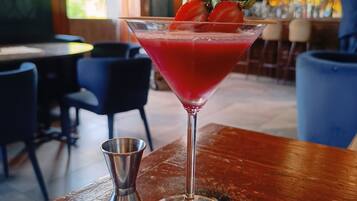 Un bar con una copa de martini que contiene un cóctel rojo adornado con fresas, un plato de bayas variadas y un coctelero sobre una mesa de madera.