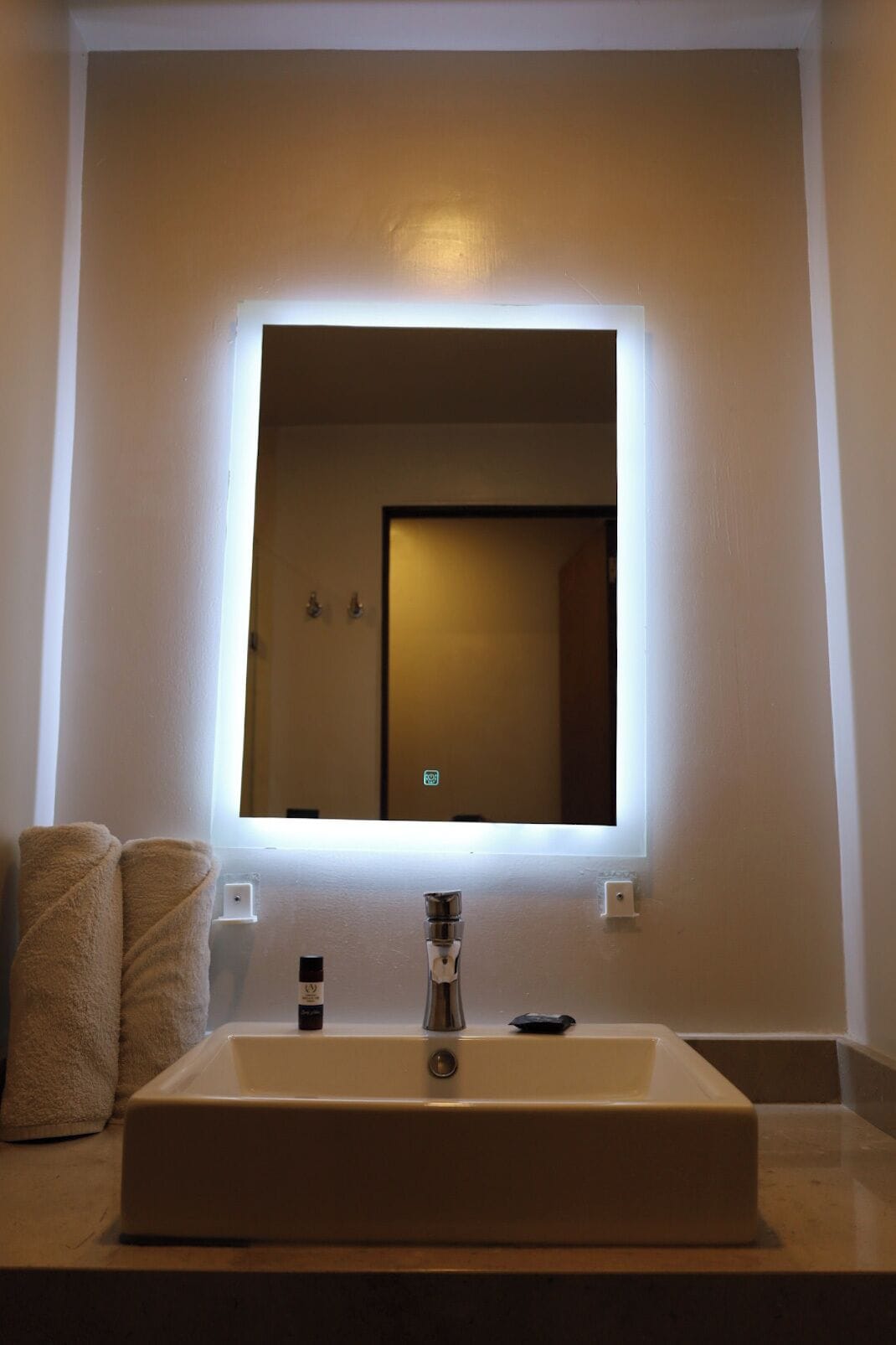 A bathroom with a large mirror, a sink, and two towels on the counter.