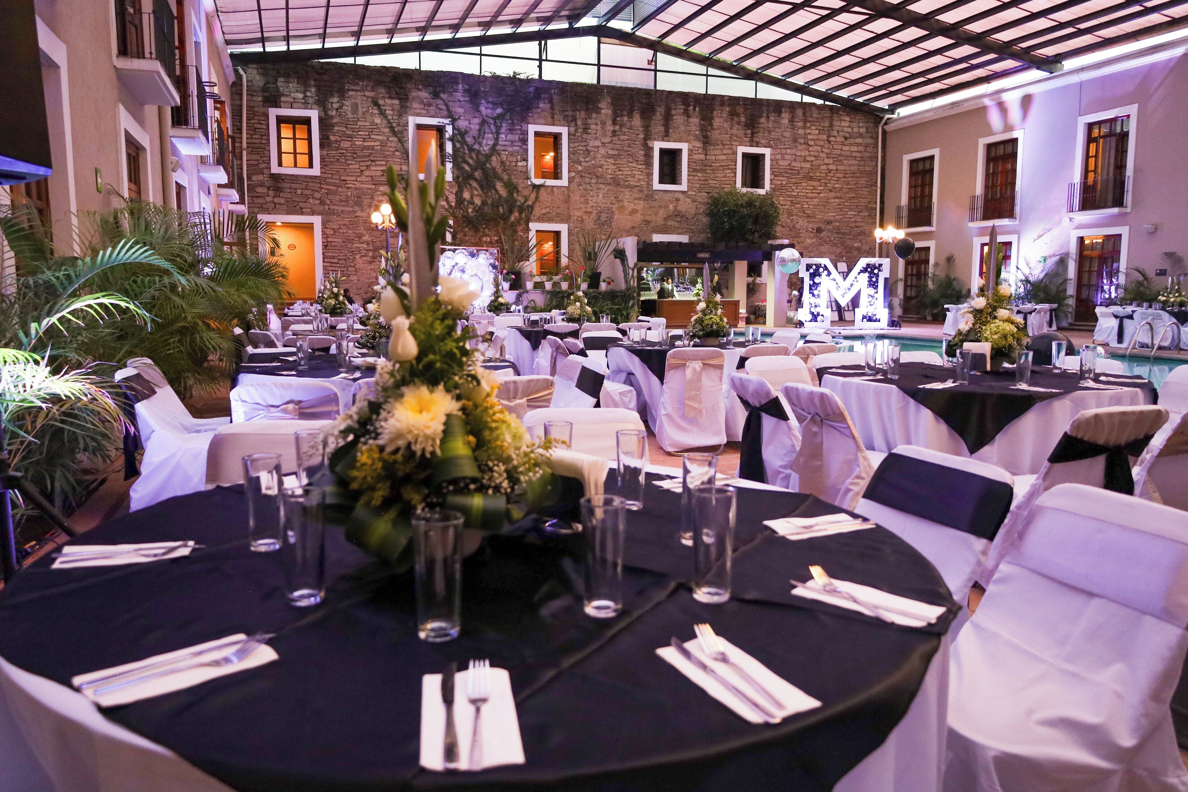 A banquet hall with round tables set for a formal event, surrounded by white chairs, and a stone building in the background.