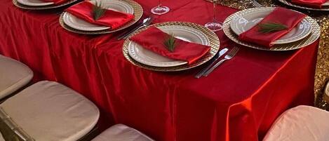 Una mesa de comedor formal con manteles rojos, platos con borde dorado y servilletas blancas.