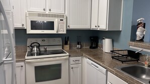 A kitchen with white cabinets, a microwave, stove, and a sink.