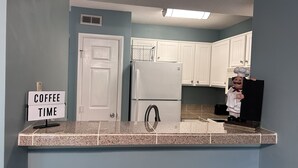 A kitchen with a sign reading "COFFEE TIME," a white refrigerator, and a chef figure.