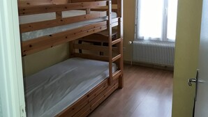 Una cama litera en una habitación con un radiador, una ventana con cortinas y una puerta.