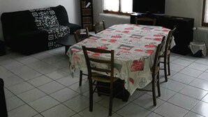 Un comedor con una mesa preparada para cuatro personas, un sofá negro, un televisor y una ventana con cortinas.