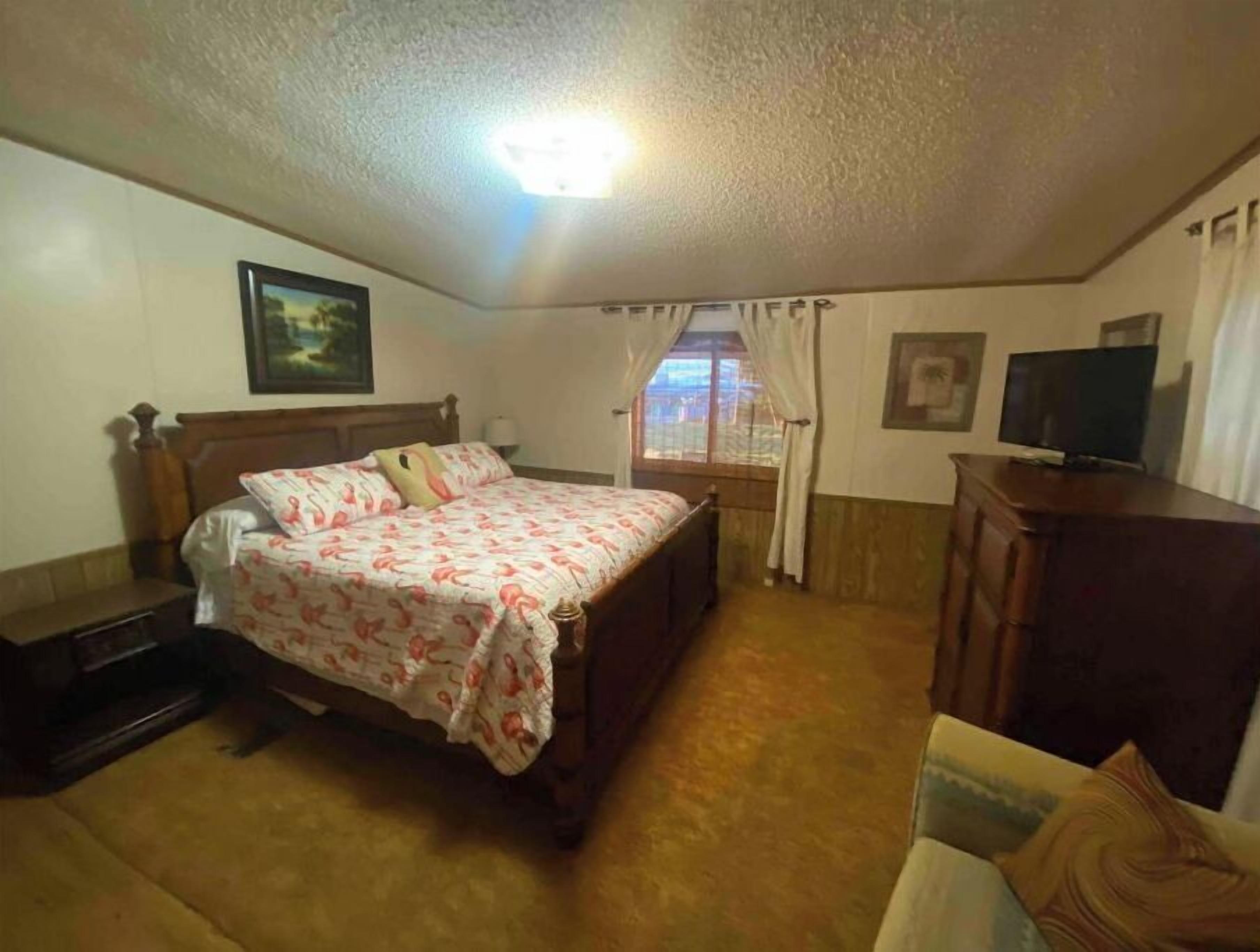 A bedroom with a bed, a TV, a desk, and a window with curtains.