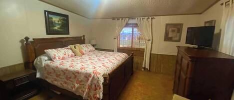 A bedroom with a bed, a TV, a desk, and a window with curtains.
