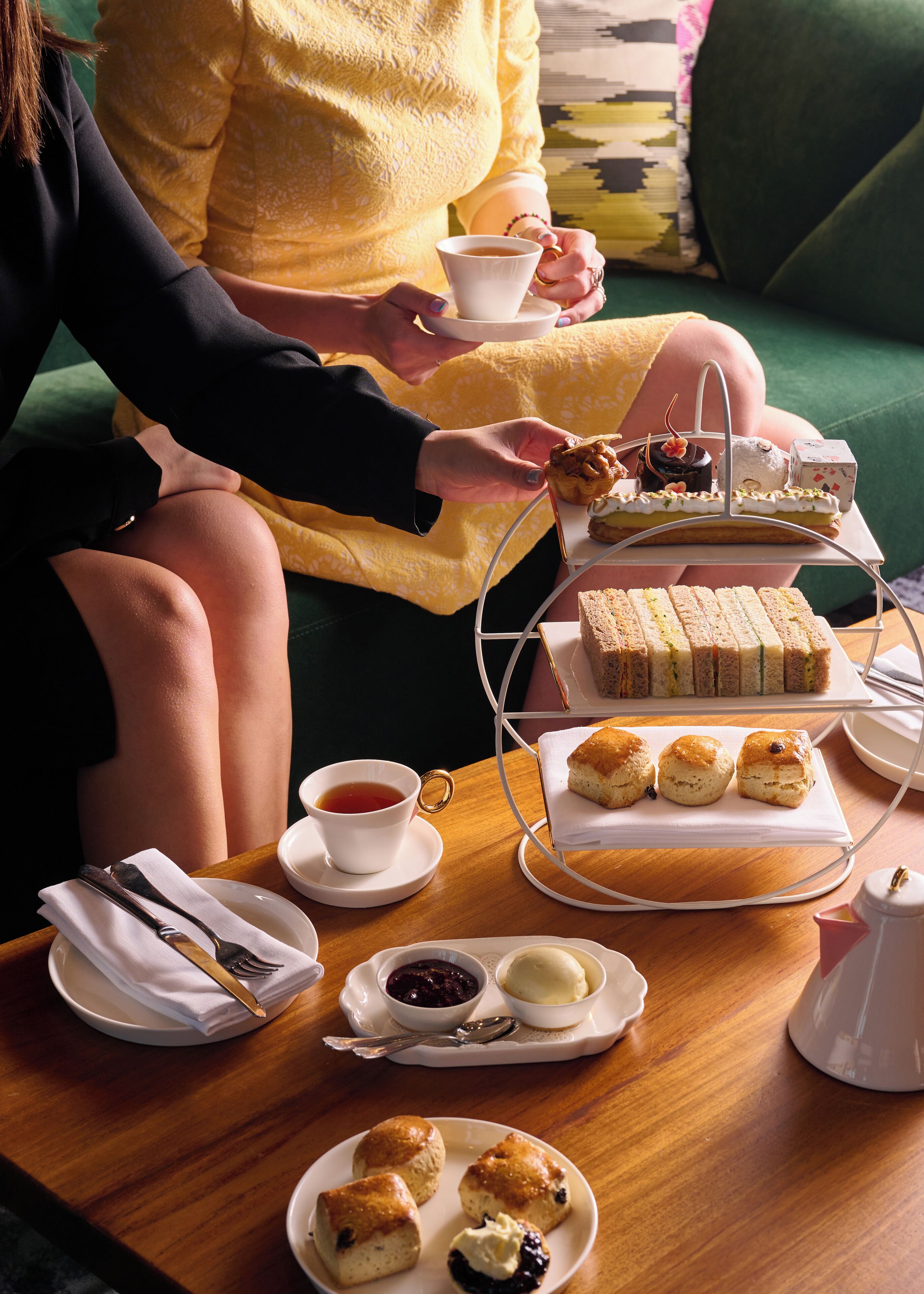 A table set with a variety of sandwiches, scones, and pastries, along with a cup of tea.